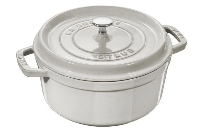 A round, white enameled cast iron cocotte with a lid and handles, labeled "STAUB" on the side.